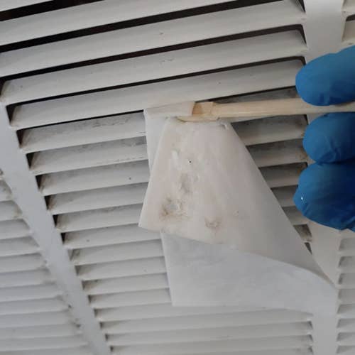 reviewer wearing gloves and using a popsicle stick and the sheet to clean inside their vent 