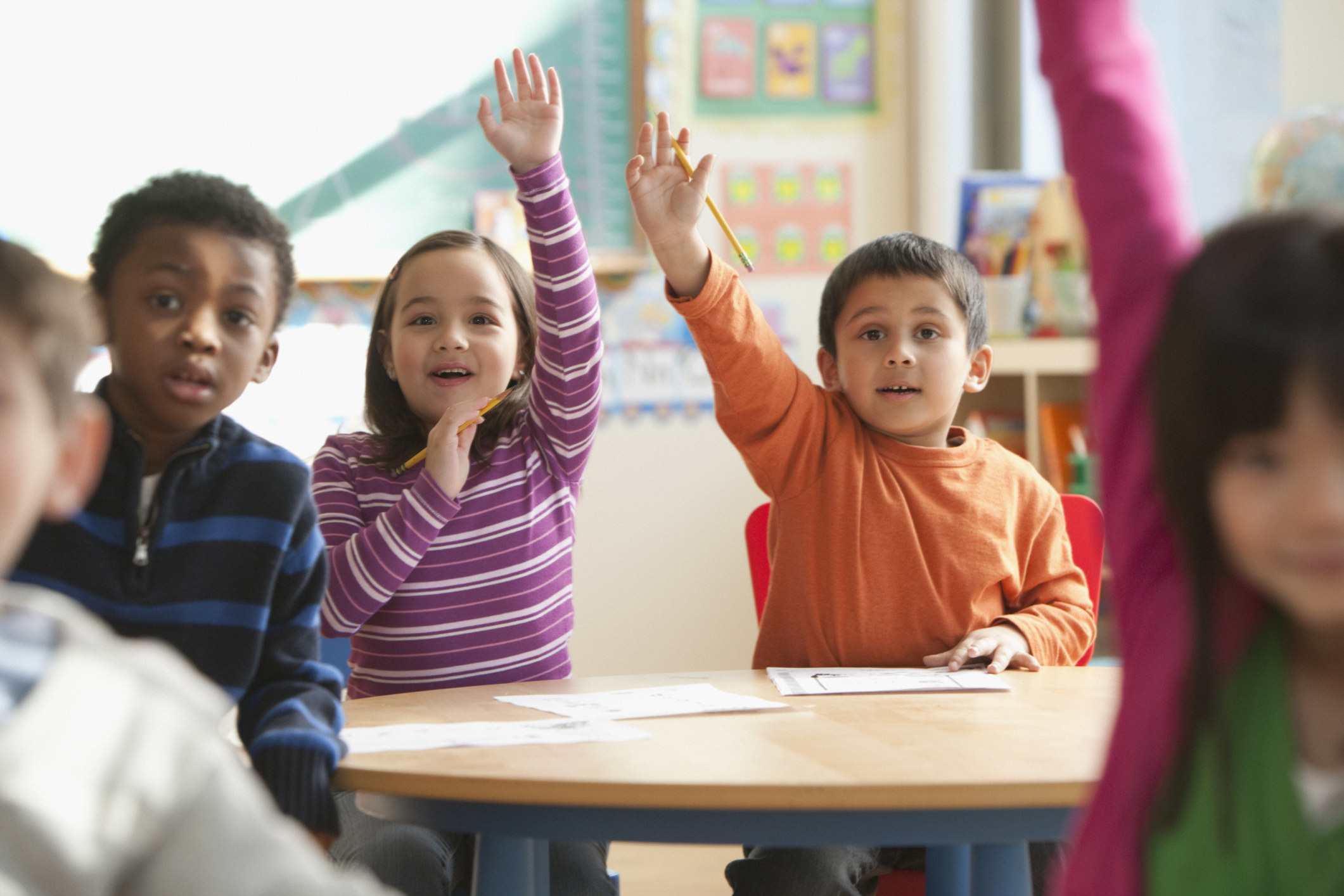 Kids in a classroom raising their hands