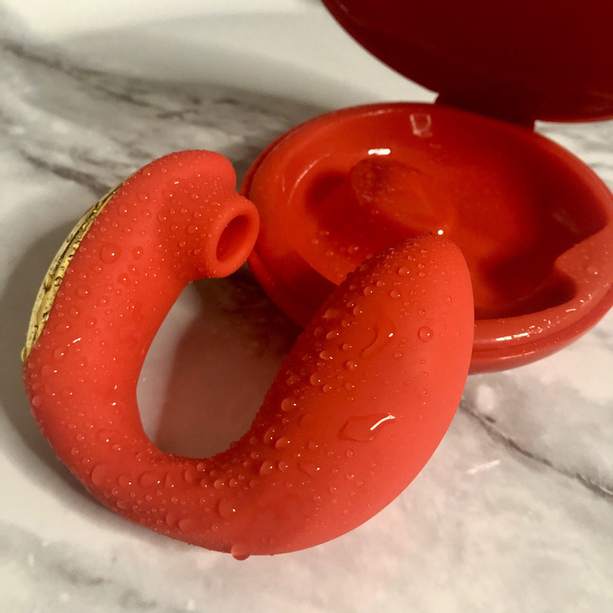 Wet red and gold vibrator next to red clamshell case