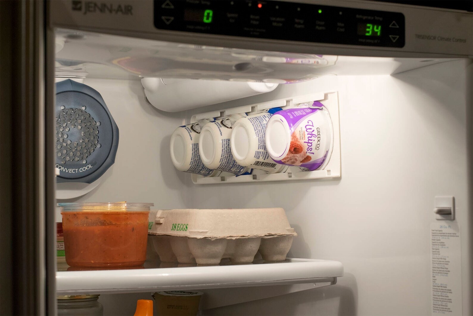 The white organizer installed on the side of the fridge wall on the inside with four yogurt cups on it