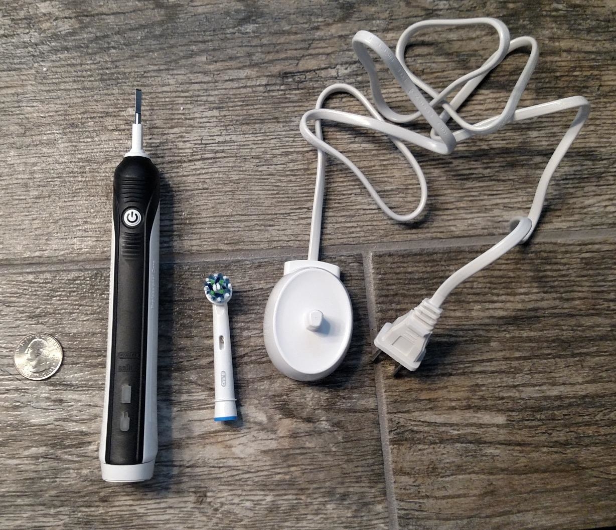 Reviewer&#x27;s electric toothbrush, brush head, and charger on floor