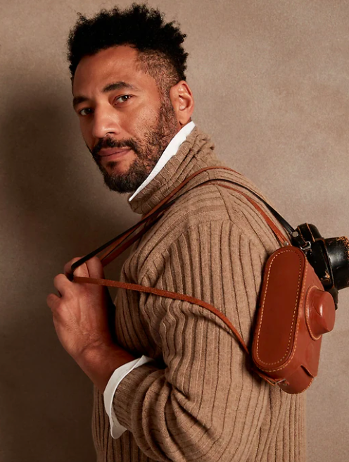 a person wearing the ribbed turtleneck over a dress shirt; a leather camera bag is slung over their shoulder