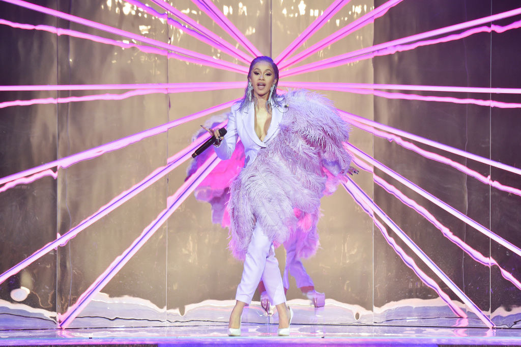 Cardi performing in a light-colored pantsuit with large feathers coming across her body