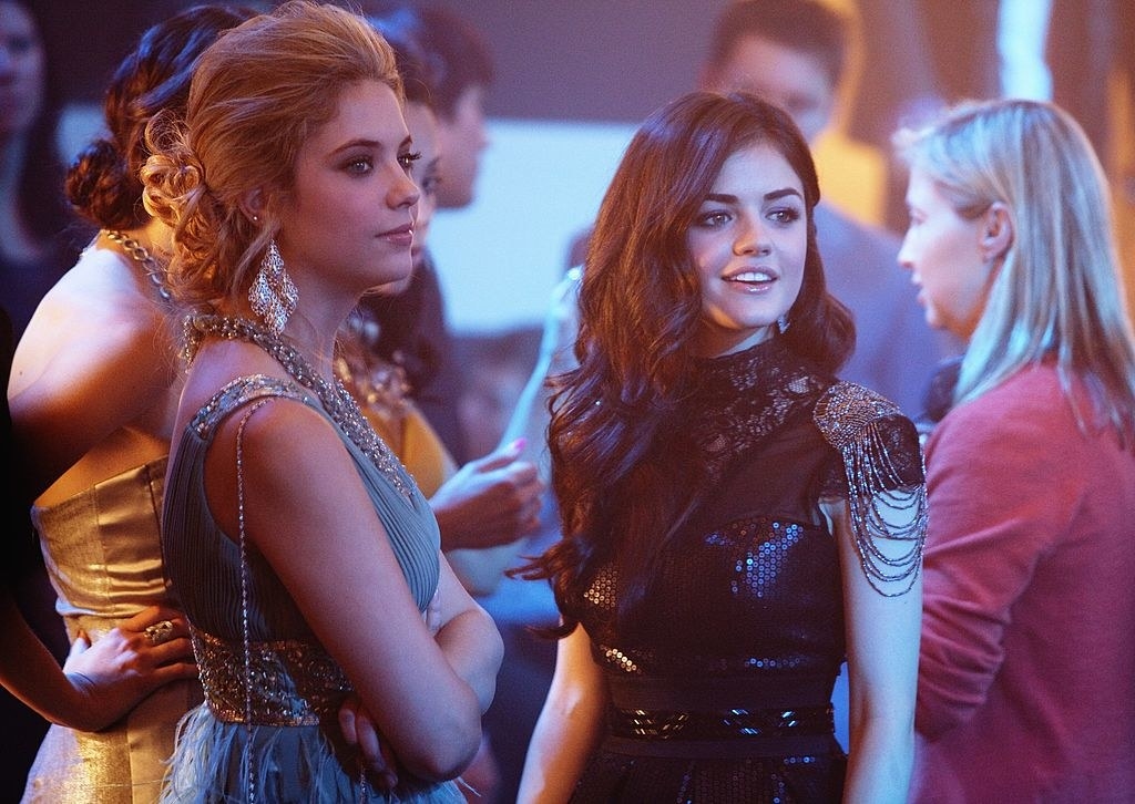 Hanna wearing a blue dress with dangling, diamond earrings and Aria wearing a black dress