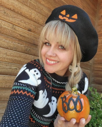 a reviewer wearing the sweater in black, posing with their halloween decor