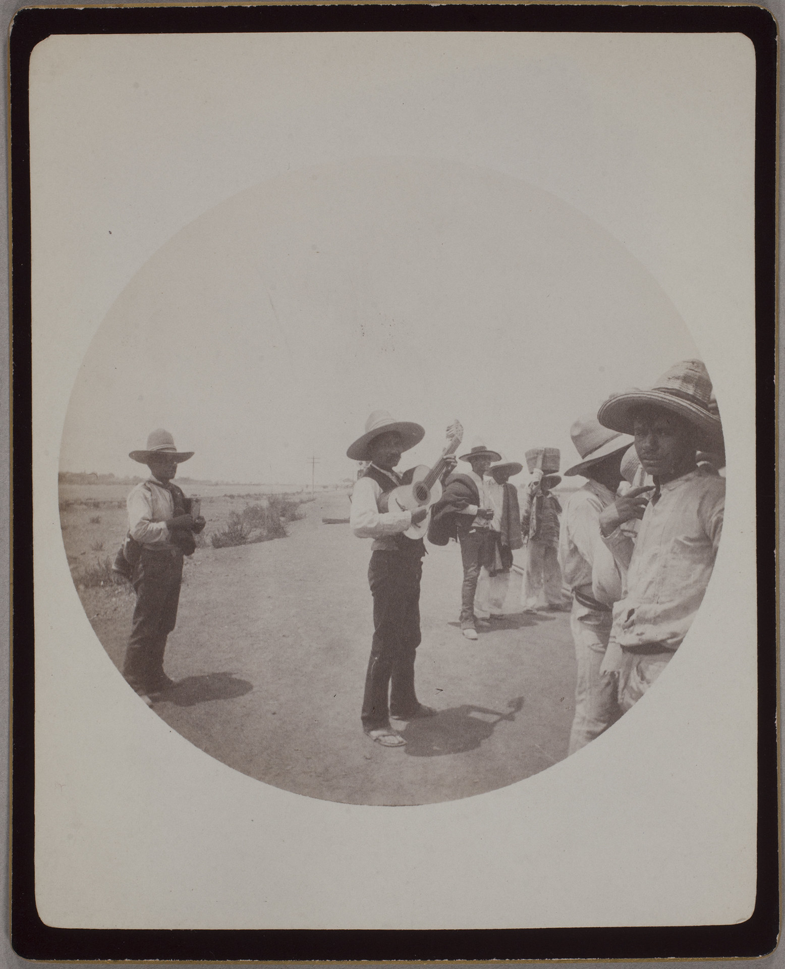 A group of men in hats, one playing guitar in the center, one looking at the camera in the far right