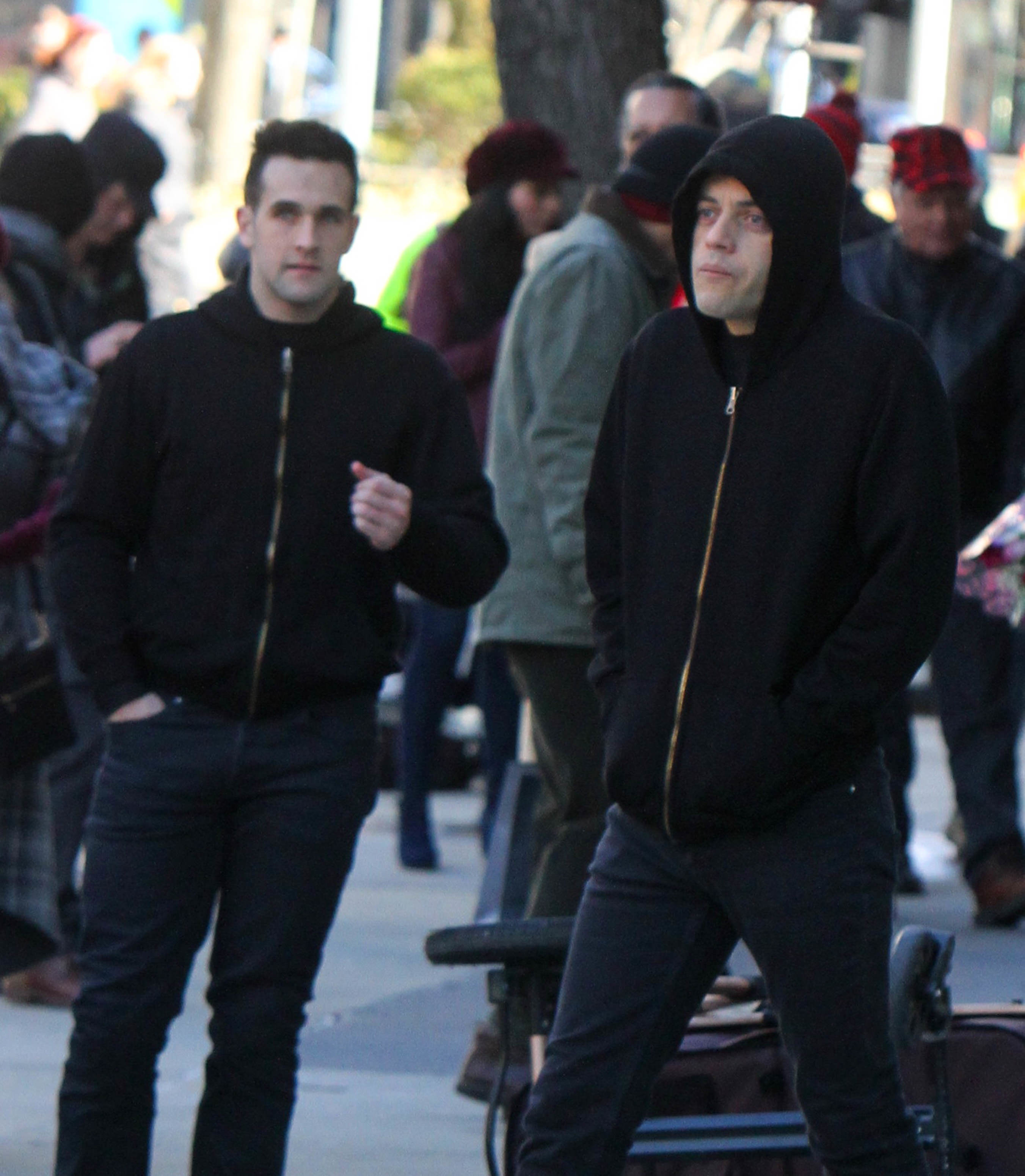 Rami Malek and his stunt double wearing black hoodies while filming