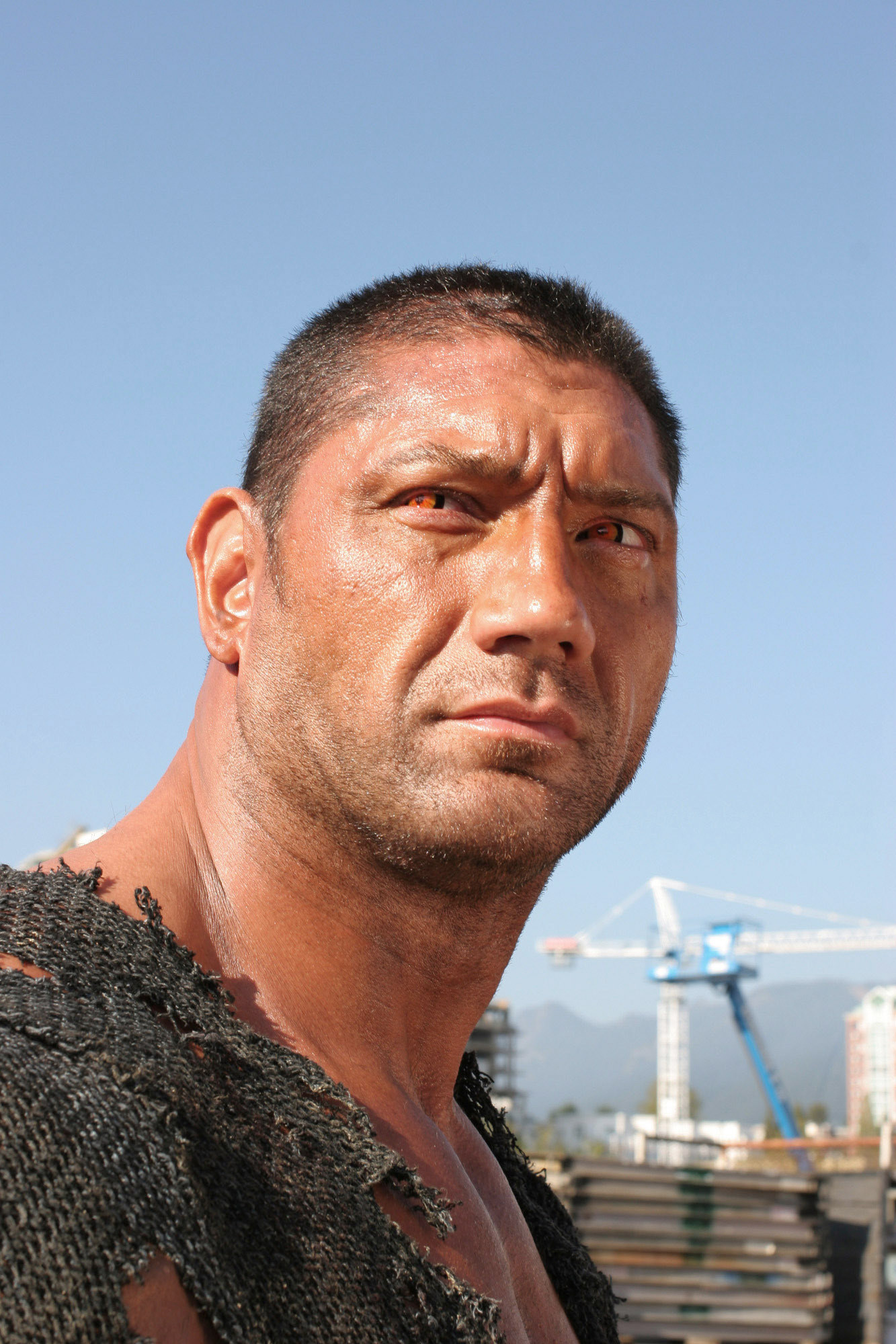 Close-up shot of Dave in &quot;Smallville,&quot; he wears orange contacts and a ripped canvas shirt, he stands in front of a construction zone that&#x27;s blurred in the background
