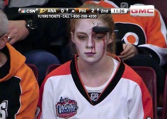 Someone with a hockey puck sticking out of their face and fake blood streaming down