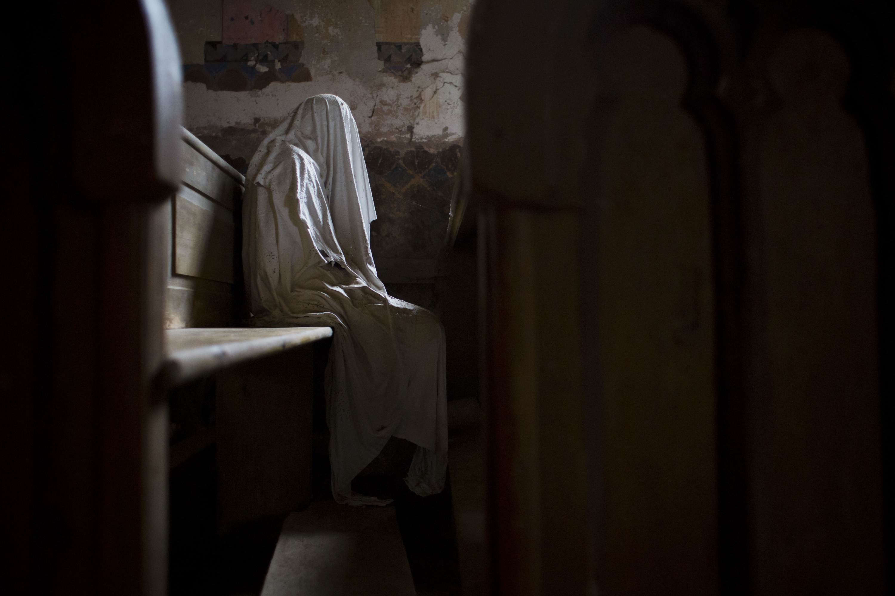 plaster ghost sitting alone in a pew against the wall at abandoned church