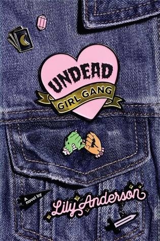 A denim jacket with enamel pins boasting the title and author name, as well as a dagger, moon and crystal and two hands pinky promising, one green with a bone sticking out.