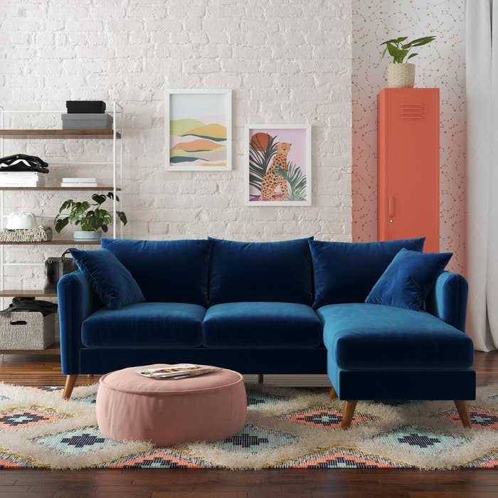 blue velvet sectional couch in a living room with a pink, blue, and beige rug and pink ottoman