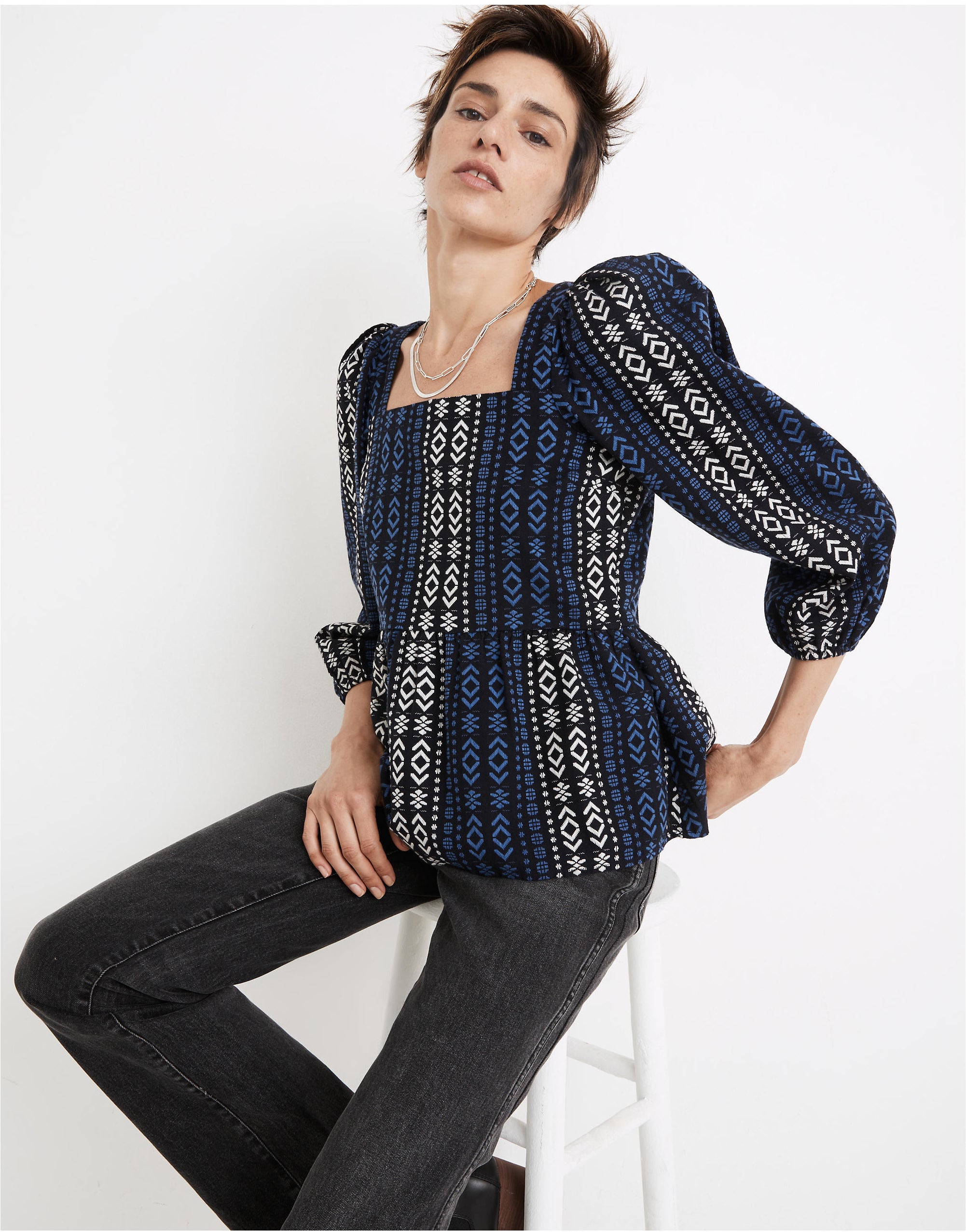 model wearing the puff-sleeve peplum top with black, blue, and white graphic vertical stripe pattern
