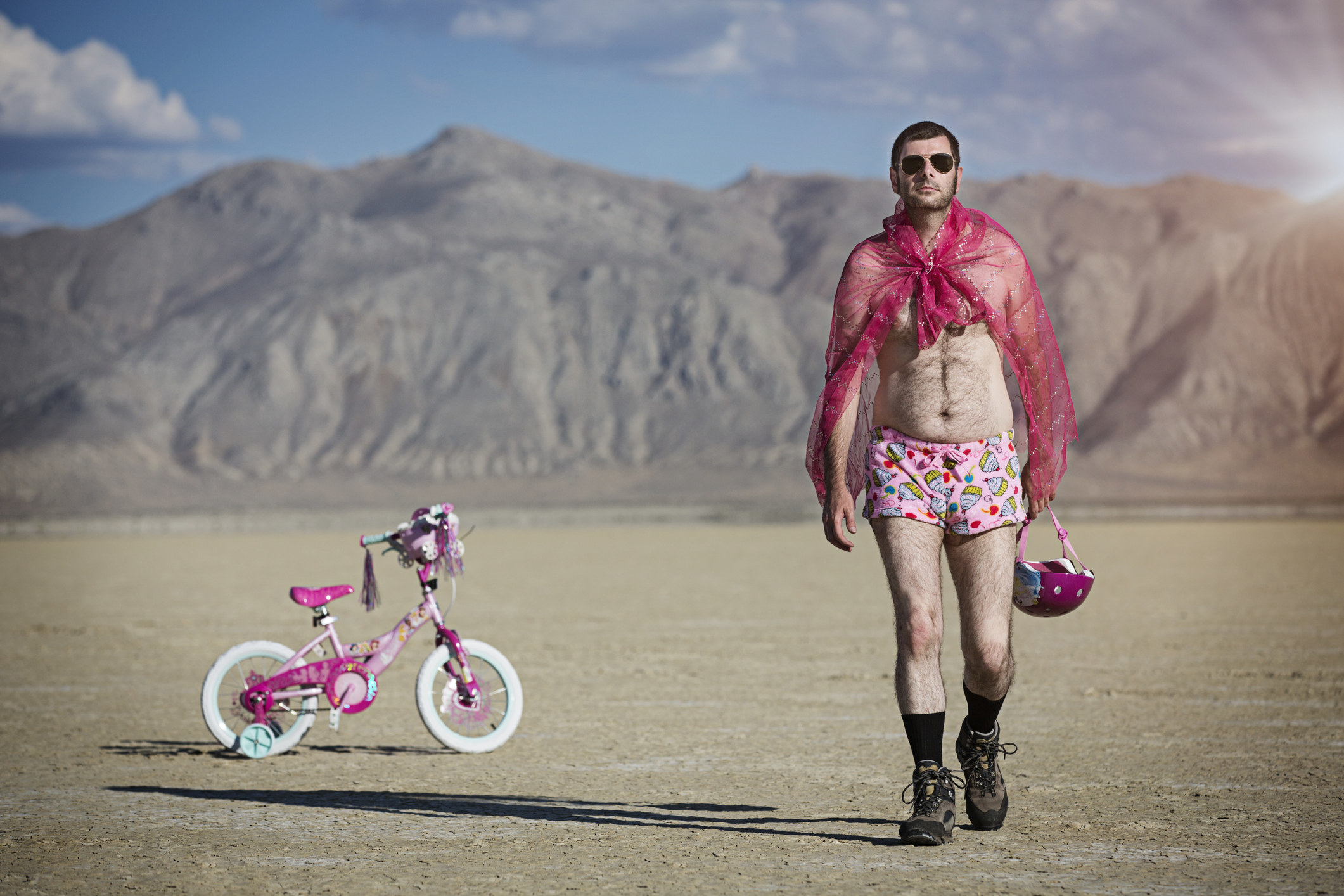 man in cape and boxers walking away from a child&#x27;s bike in the desert