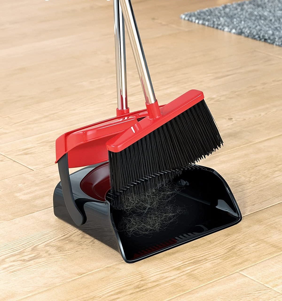 An upright broom and dustpan where the dustpan has dirt-removing teeth around the rim