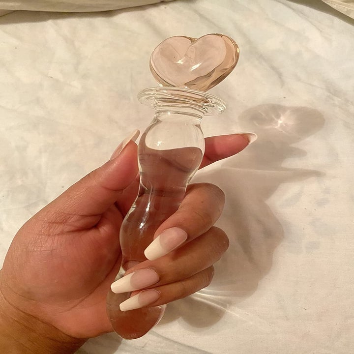 A reviewer holding the glass dildo with a pink heart on one end
