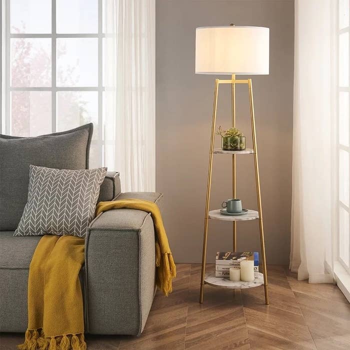 A three-tired lamp  with a plant, mug, and stacked books.