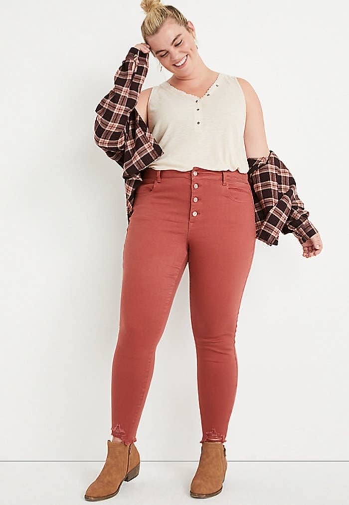 model wearing the red pants with brown boots and a white tank top with a flannel jacket on top