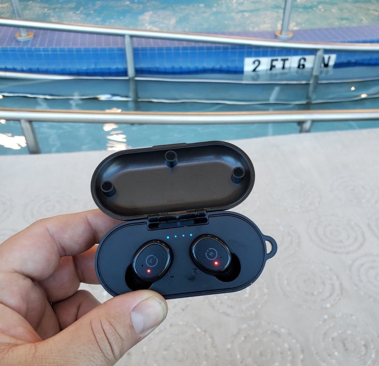 Reviewer photo of them holding the earbuds in its charging case in front of a pool
