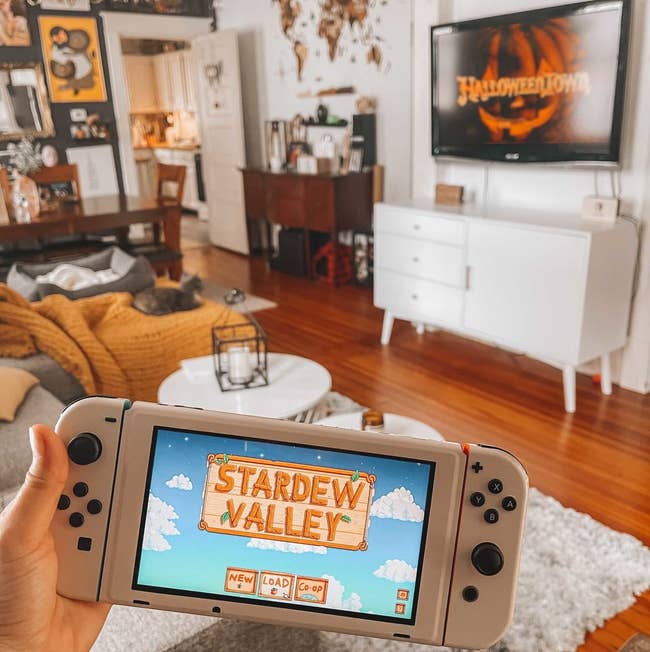 The writer is holding her Nintendo Switch with her living room in the background, the switch is covered in a cream skin