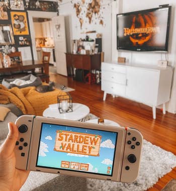The writer is holding her Nintendo Switch with her living room in the background, the switch is covered in a cream skin