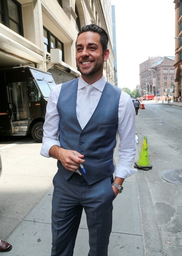 Zachary Levi posing in the middle of the street wearing a vest suit and holding a sharpie