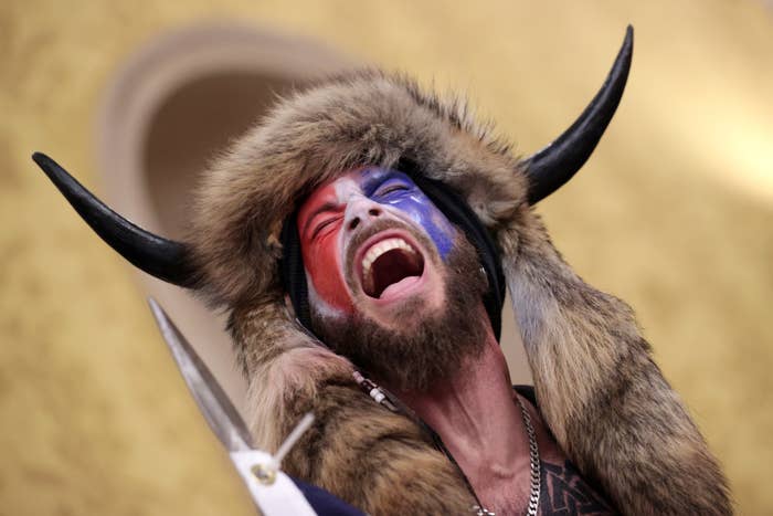 A man wearing face paint, an animal hide over his head, and horns screams