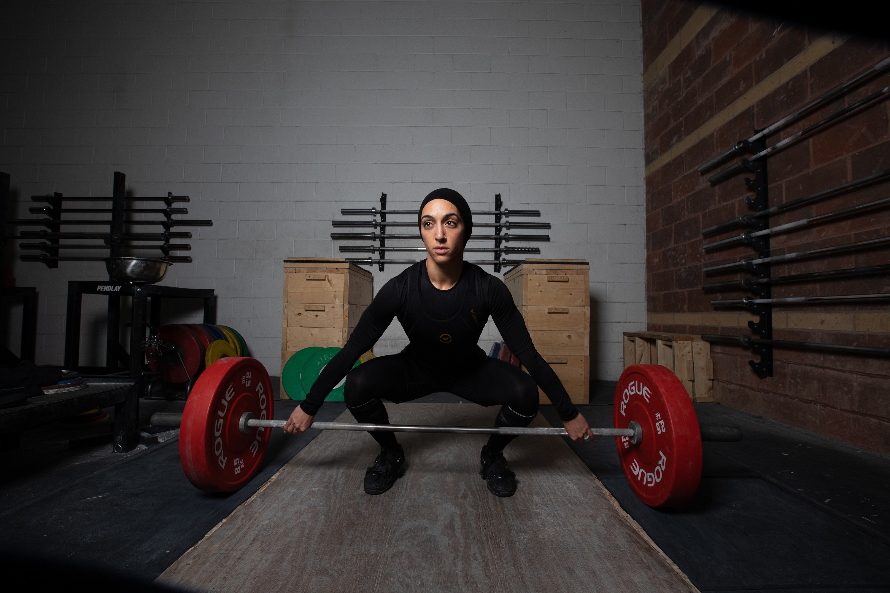 A woman with her hair covered and wearing full body workout gear lifts weights in a gym