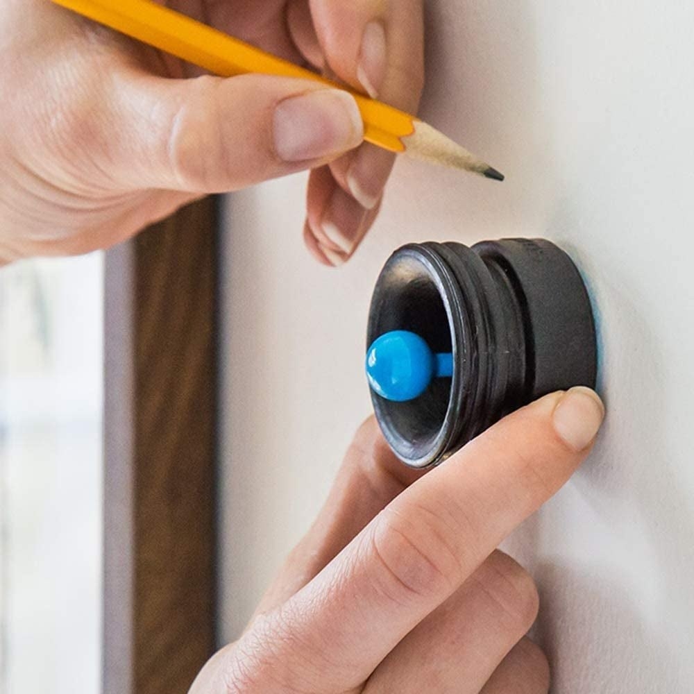 hand using the small round tool with blue knob against a wall