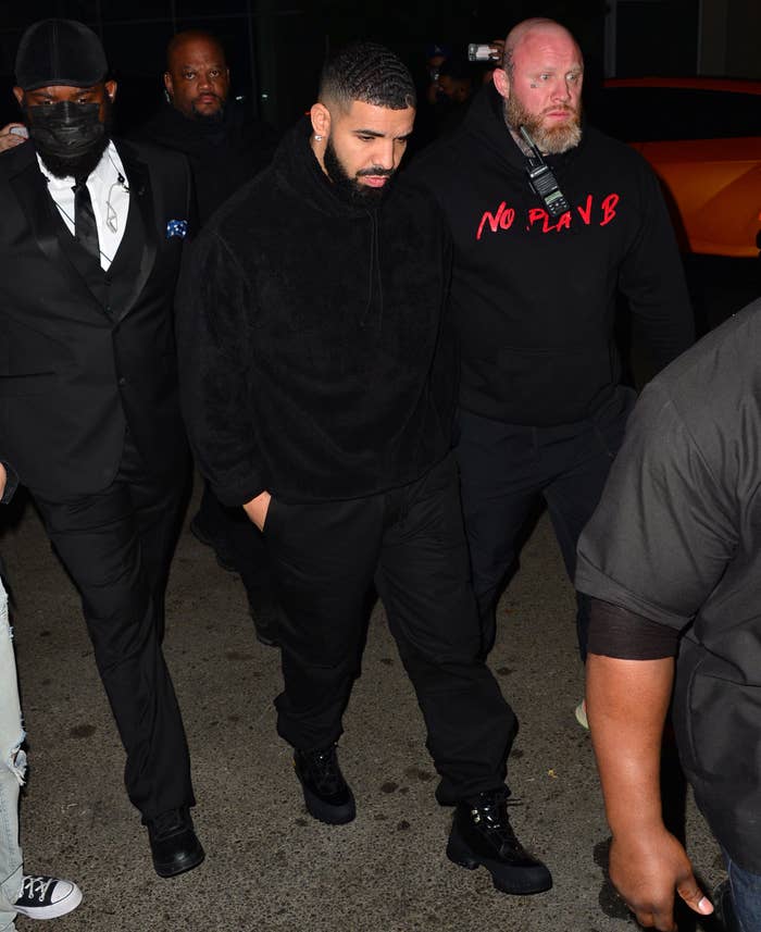 Drake walking outside surrounded by men