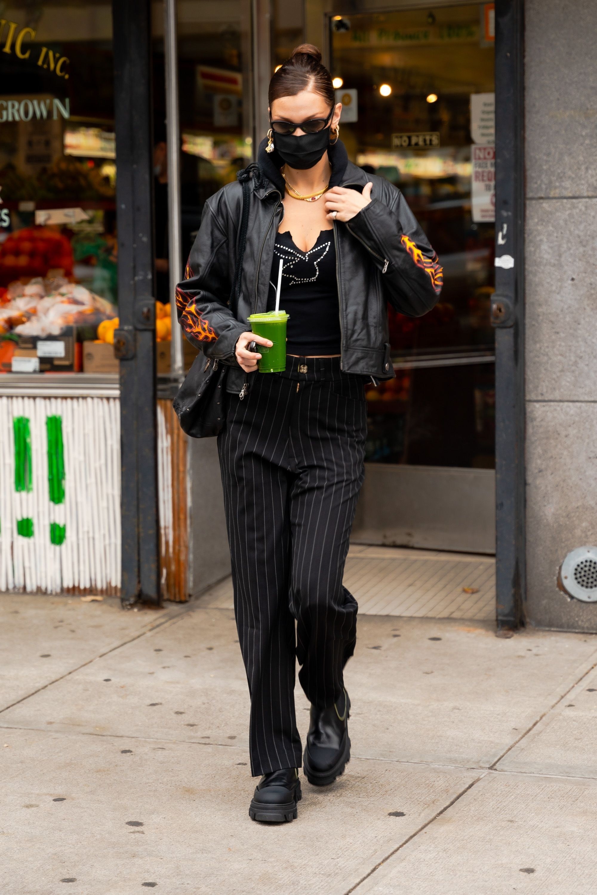 Bella Hadid in a leather jacket and striped pants holding a green juice