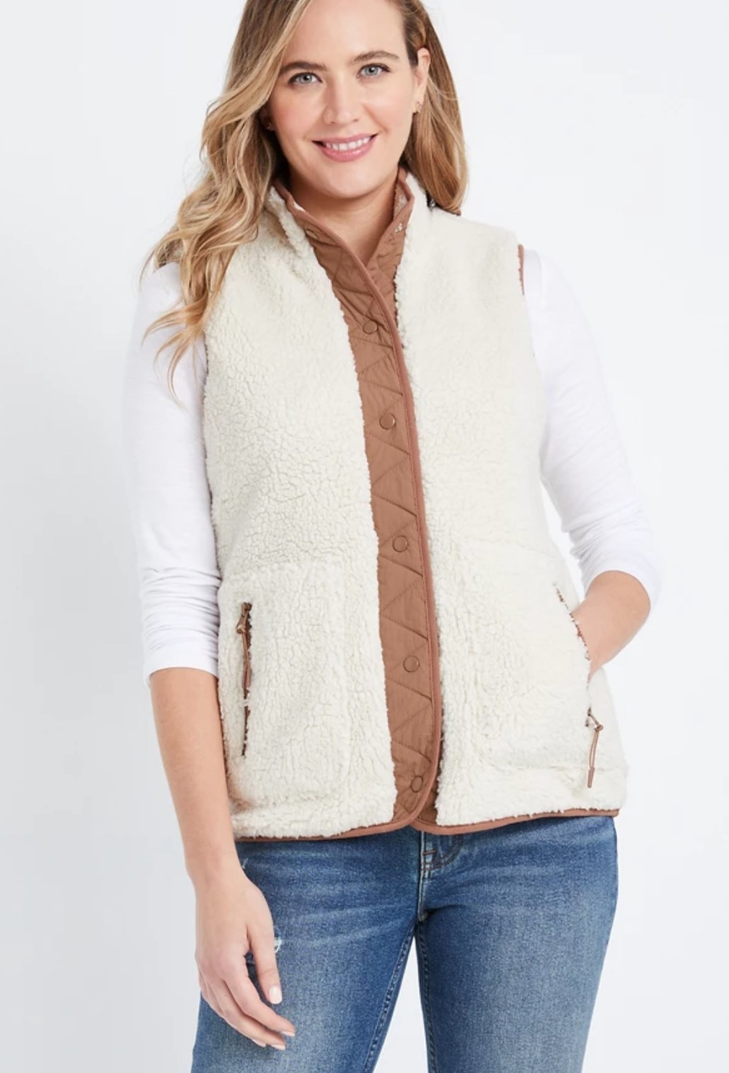 model wearing the white sherpa vest with brown trimming and blue jeans