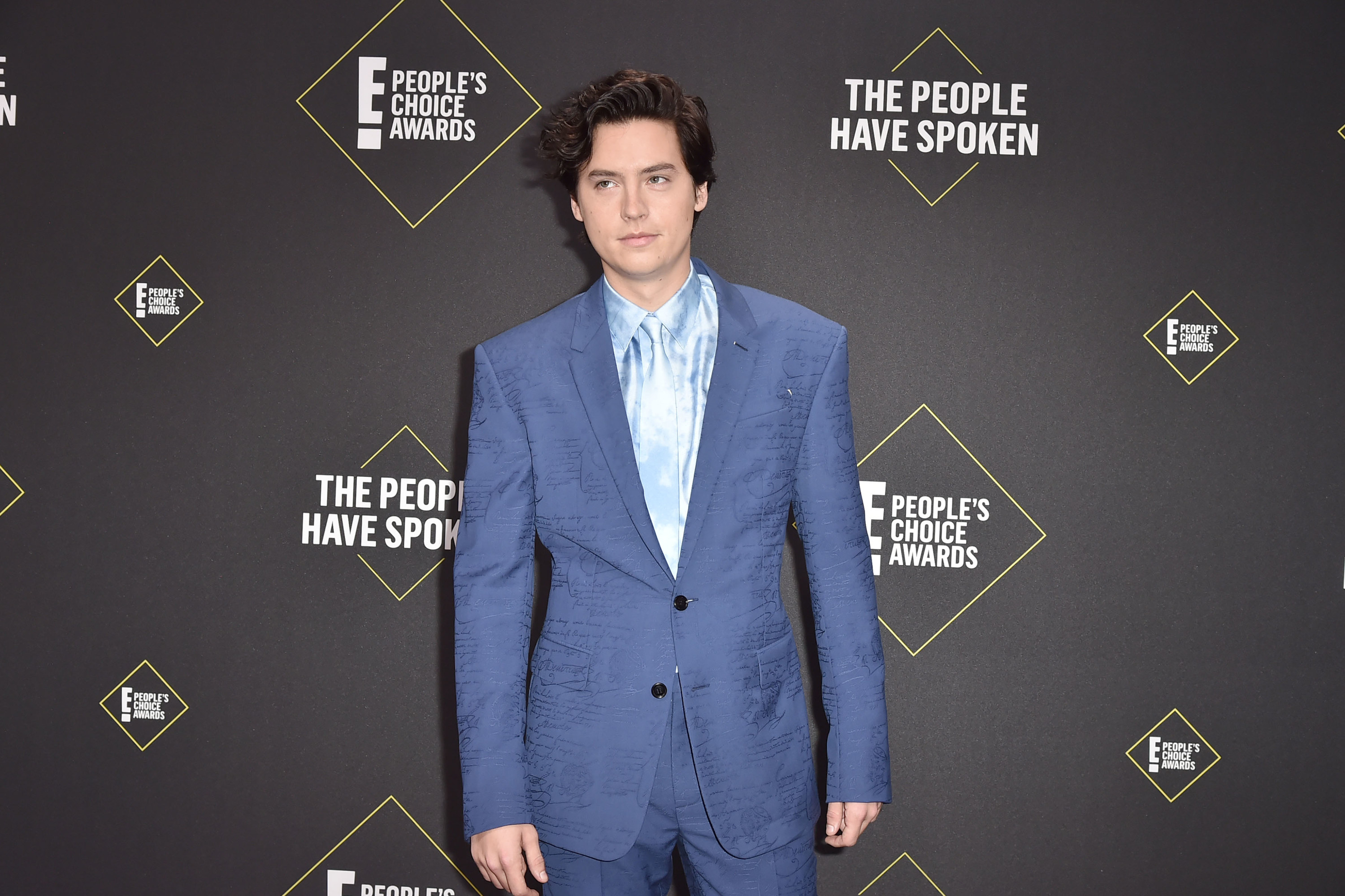 Sprouse poses for a photo on the red carpet while wearing a suit