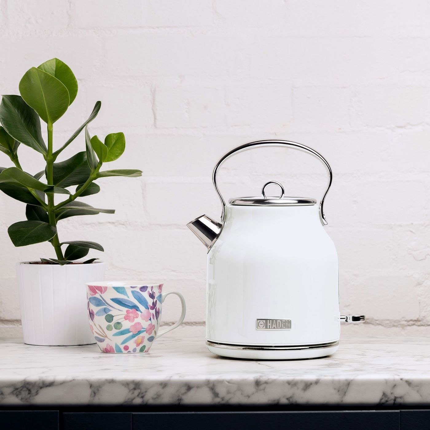the white kettle on a counter with a mug and plant