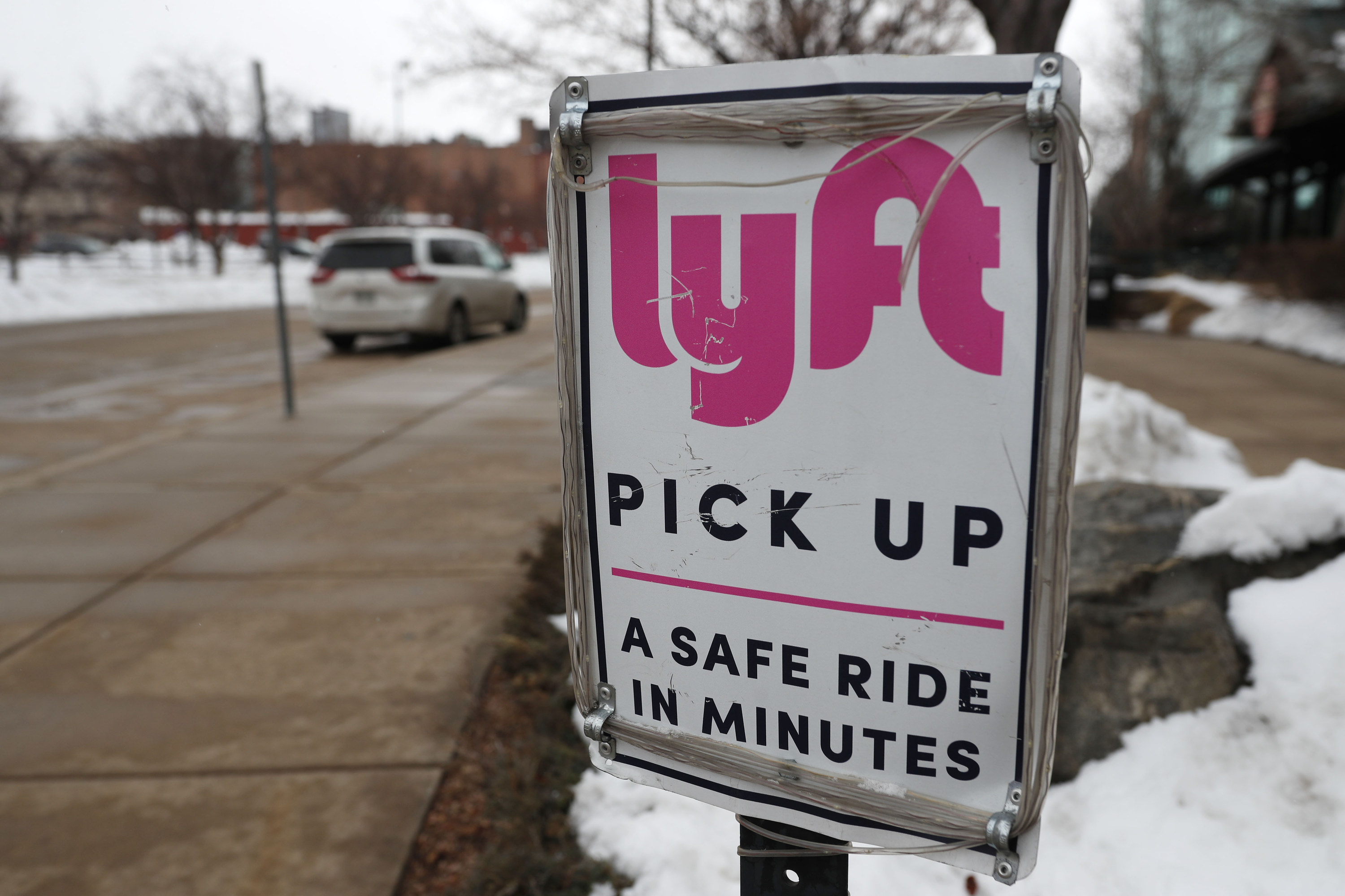 A sign posted next to a sidewalk reads &quot;Lyft pickup — a safe ride in minutes&quot;