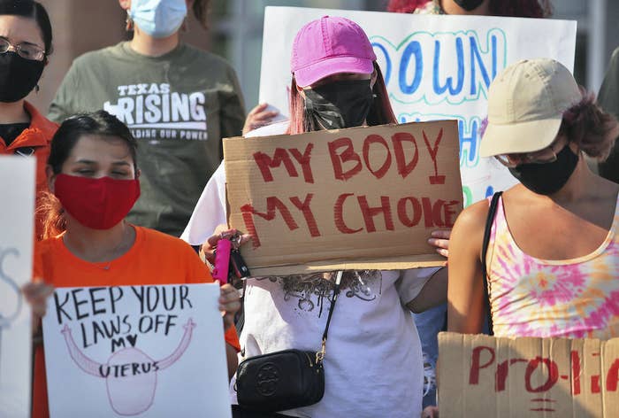 Three women hold handmade signs that read "keep your laws off my uterus" and "my body my choice"