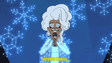 A woman in a white wig and a gown covered in twinkling lights sings into a microphone saying, &quot;Twinkling lights...shine&quot;