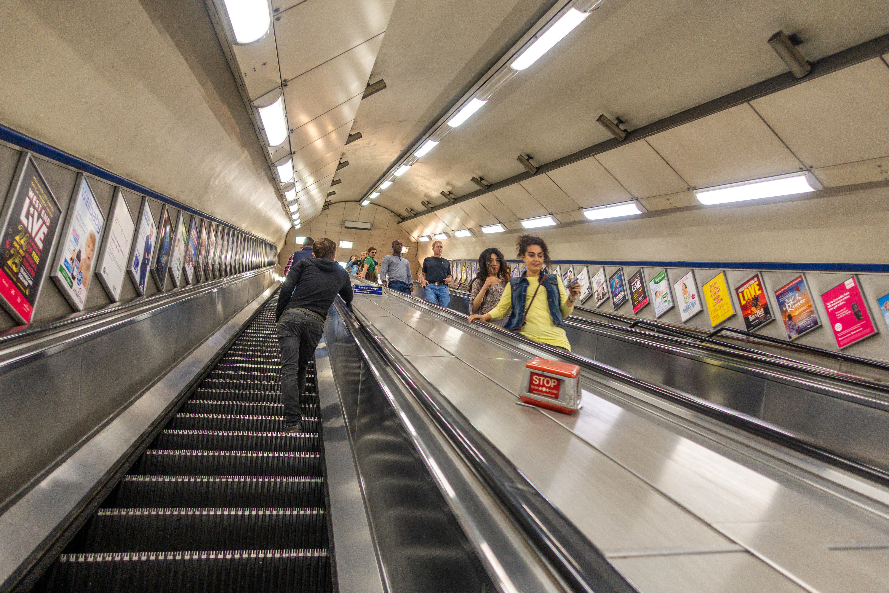 View of both the up and down escalator peppered with people standing to the right from the London tube