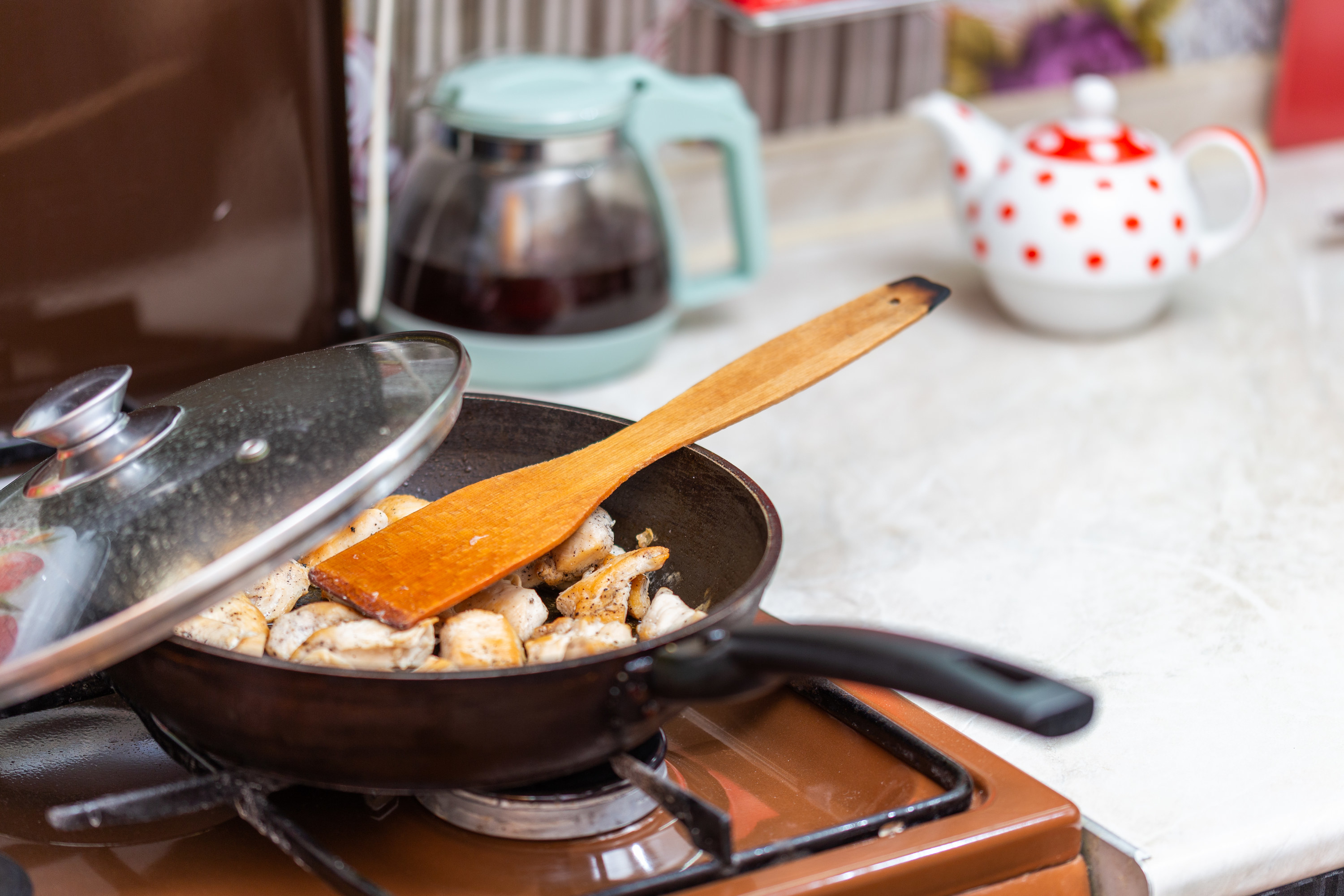 A pan with pieces of skinless chicken in it topped with a wooden spatula, handle facing forward off the stove