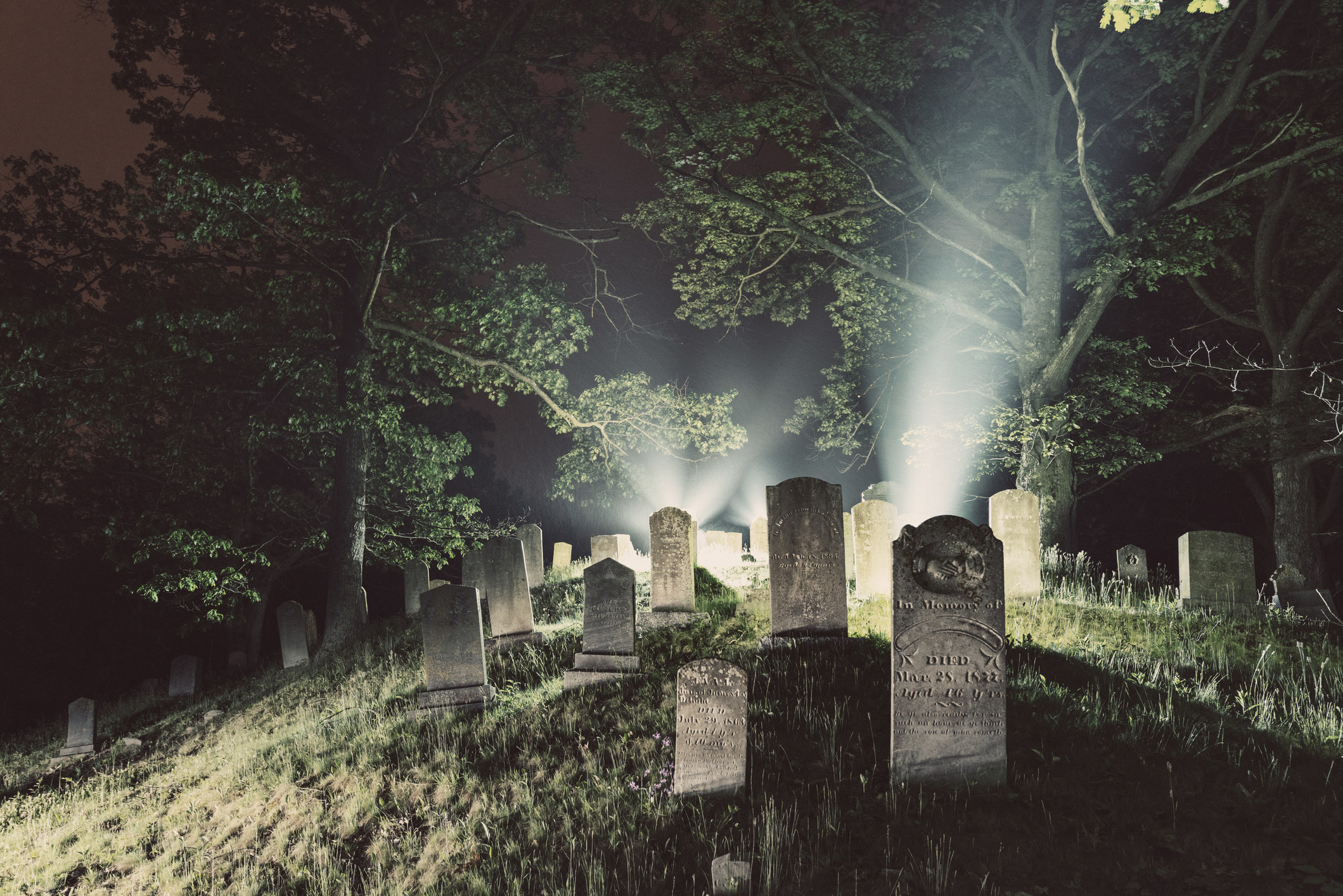 headstones on a hill at night with flashlights shining on them in the background