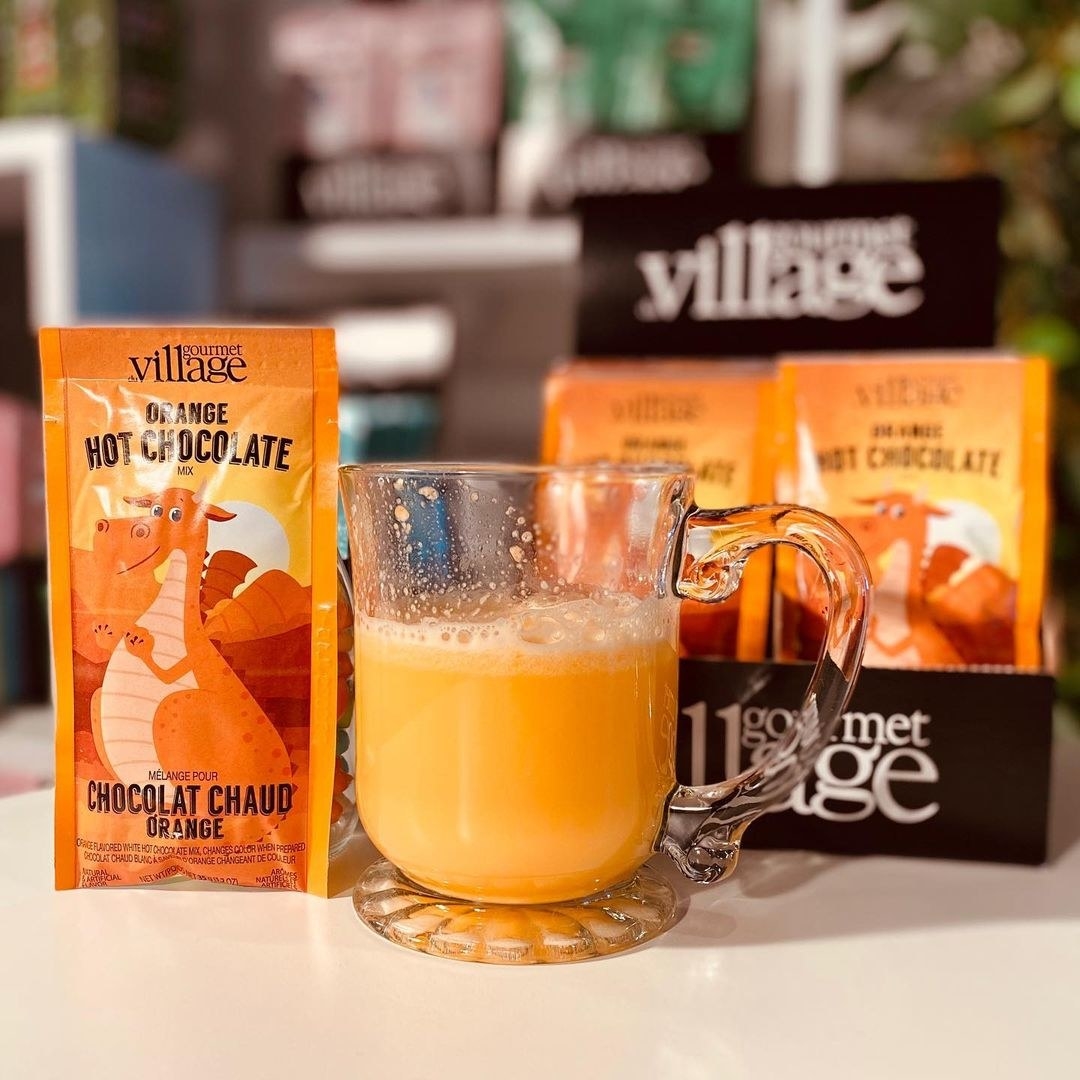 A mug of orange hot chocolate surrounded by packages of the mix