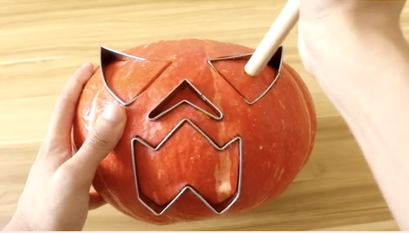 person using the molds on a pumpkin with the hammer
