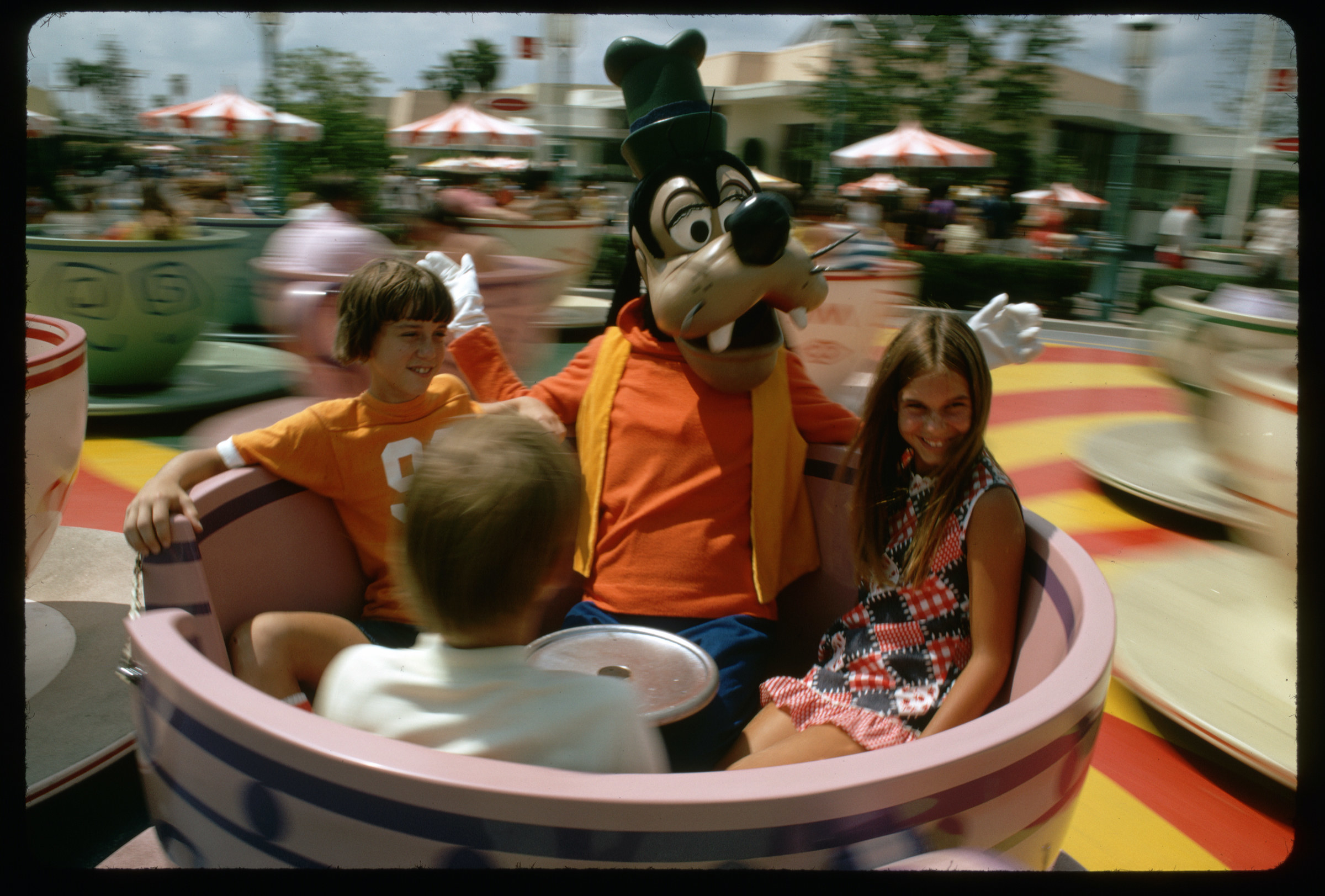 Three children enjoy a ride at Disney World with Goofy the Disney character