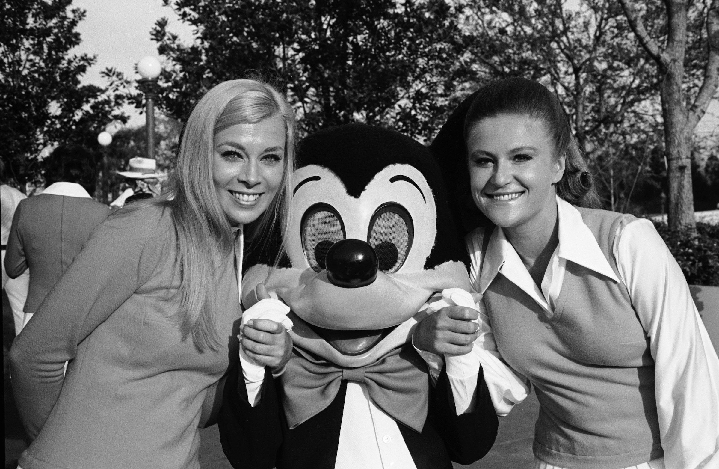 Mickey Mouse stands between two females who hold his hands for a photo