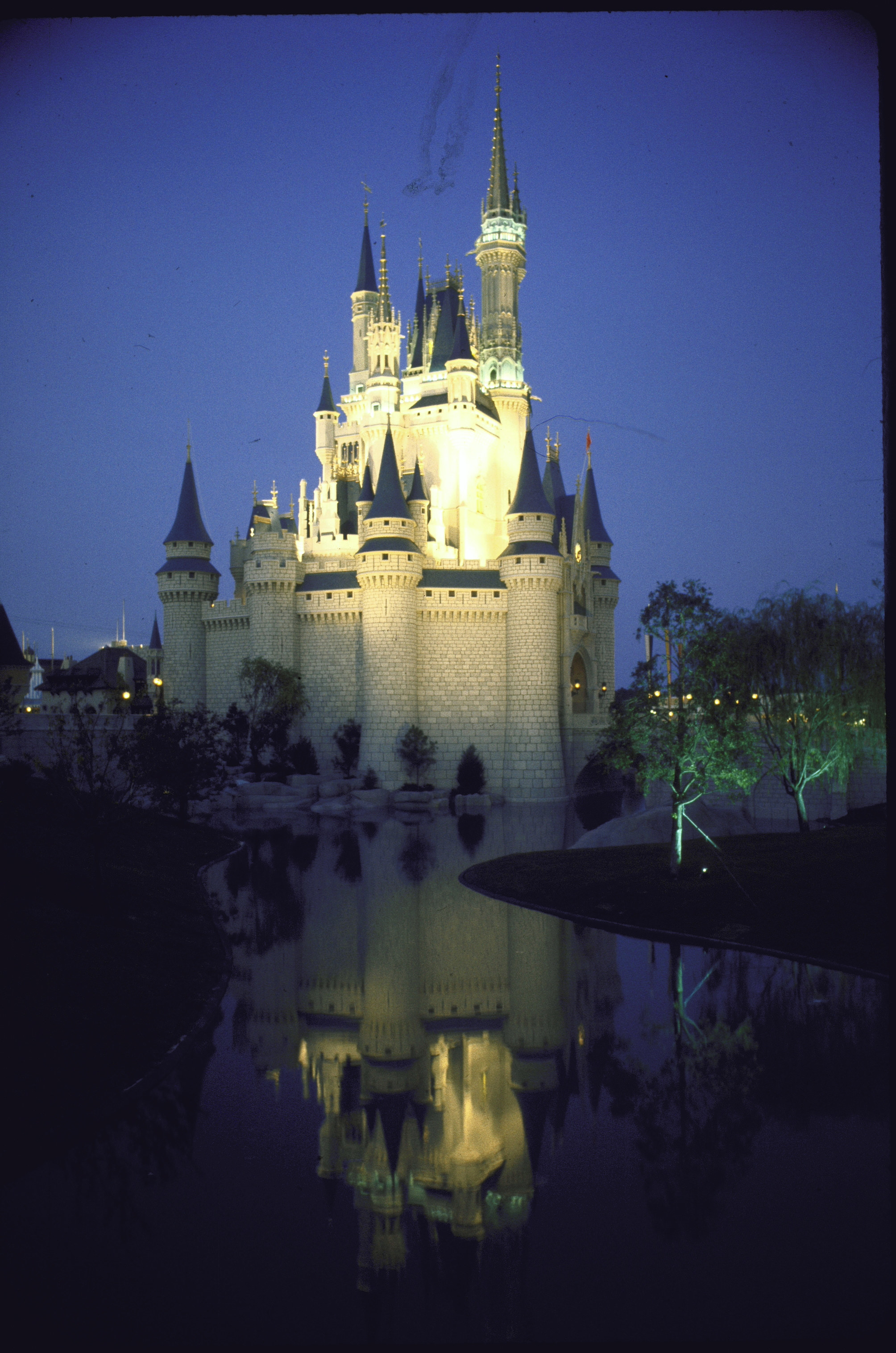 Cinderella&#x27;s Castle lit up at night and reflected in an artificial stream at Disney World