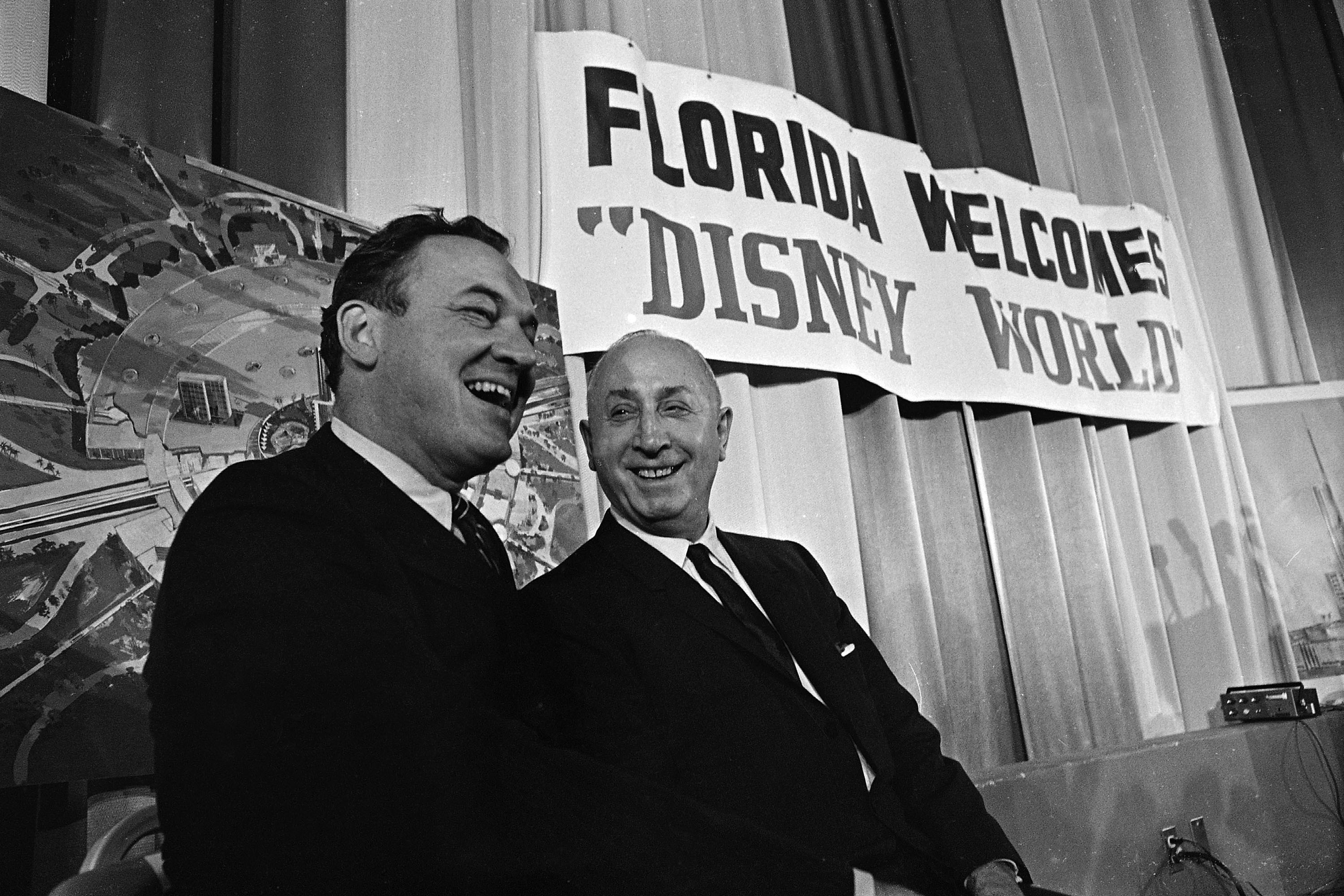 Two men dressed in suits - one the governor of Florida and the other Roy Disney - hold a press conference to announce the opening of Disney in Florida