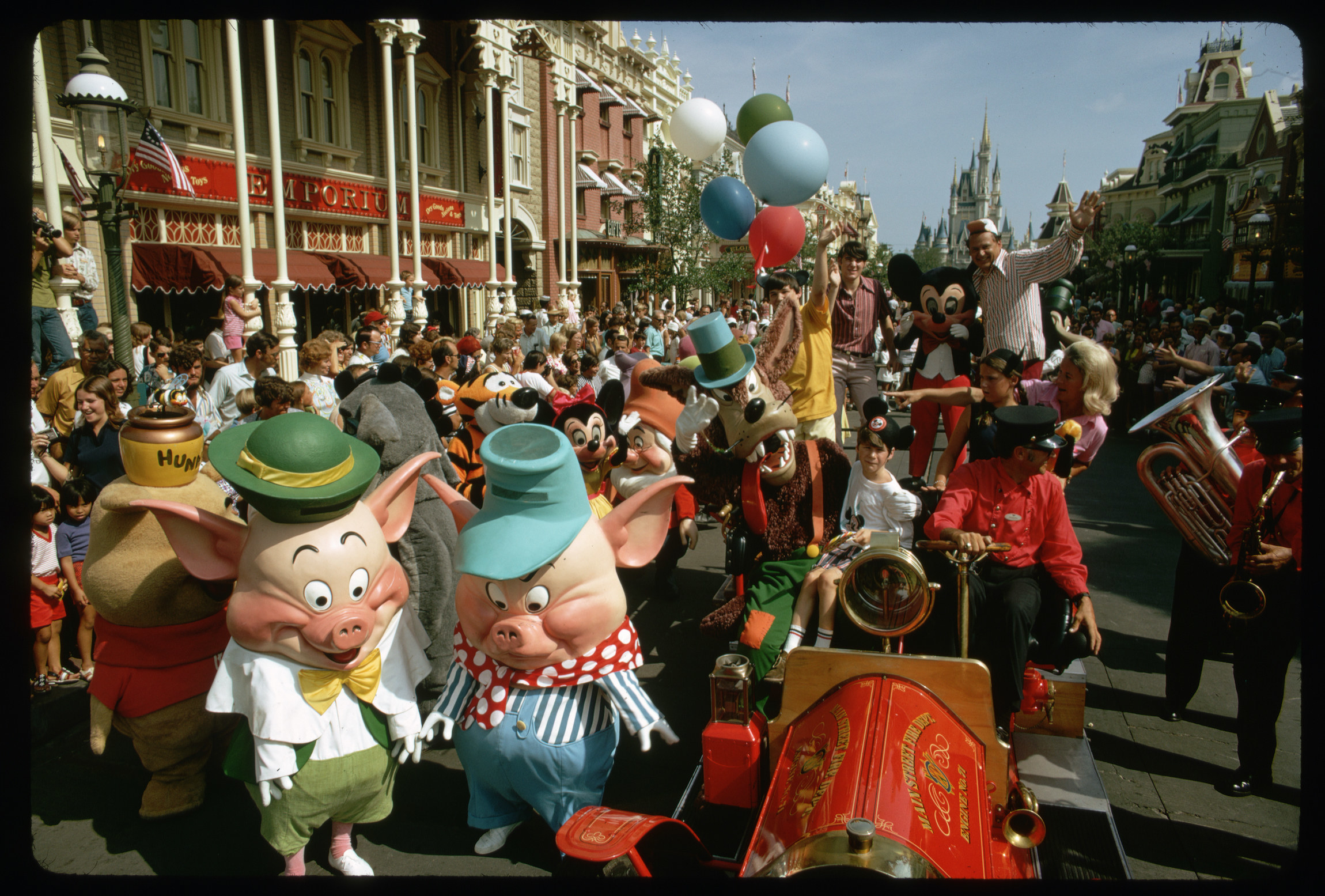 Disney characters and tourists fill a street in a parade