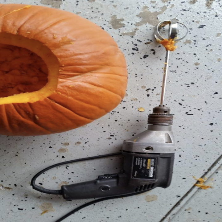 the drill attachment on a drill beside of a hollowed out pumpkin