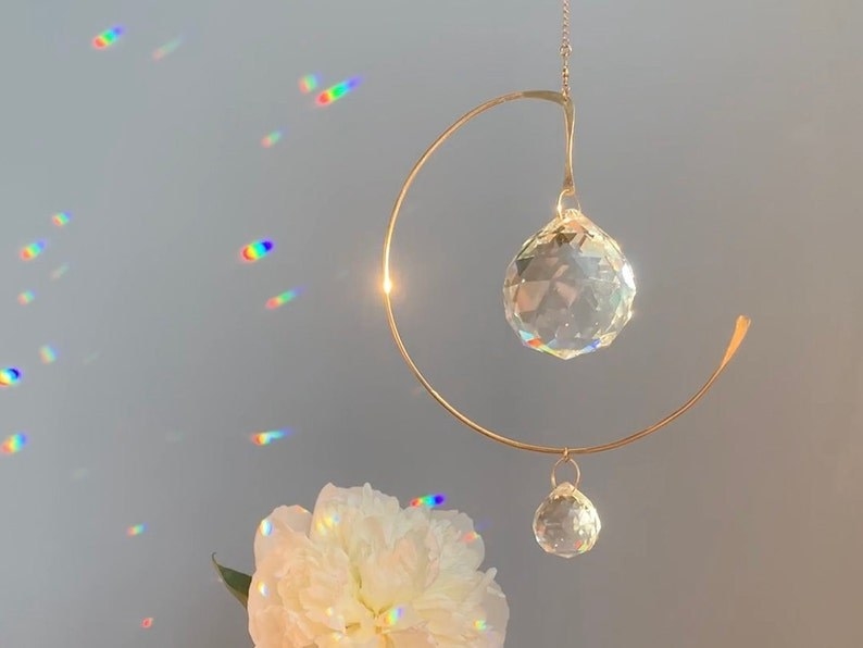 the hanging light catcher which has a gold metal piece that&#x27;s like a half-circle with a prism hanging in the top middle which looks like a round crystal and another smaller one hanging from the bottom of it
