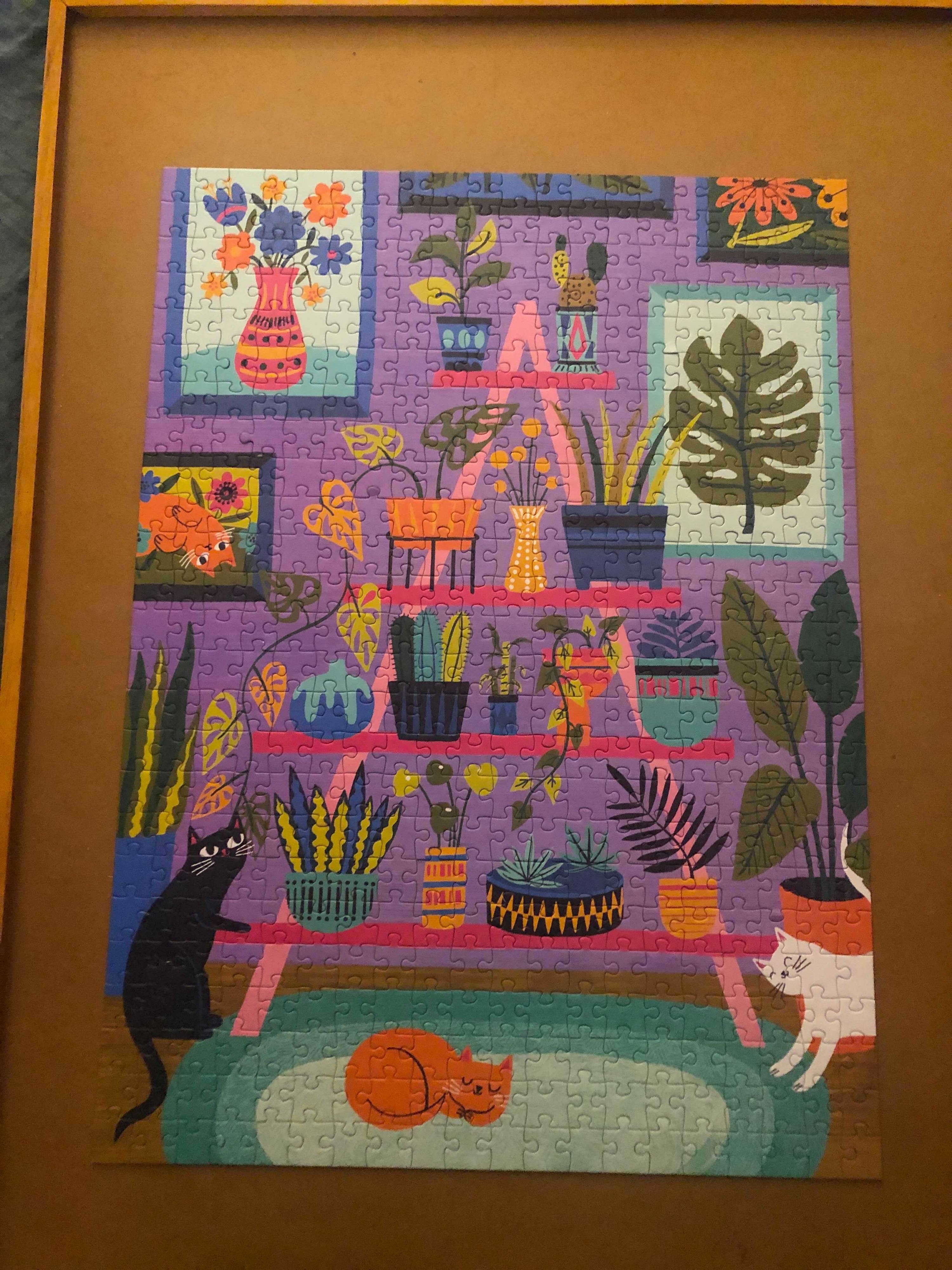 a completed puzzle with an illustration of three cats that are black, while and orange standing and laying near a plant stand that&#x27;s brimming with different kinds of plants